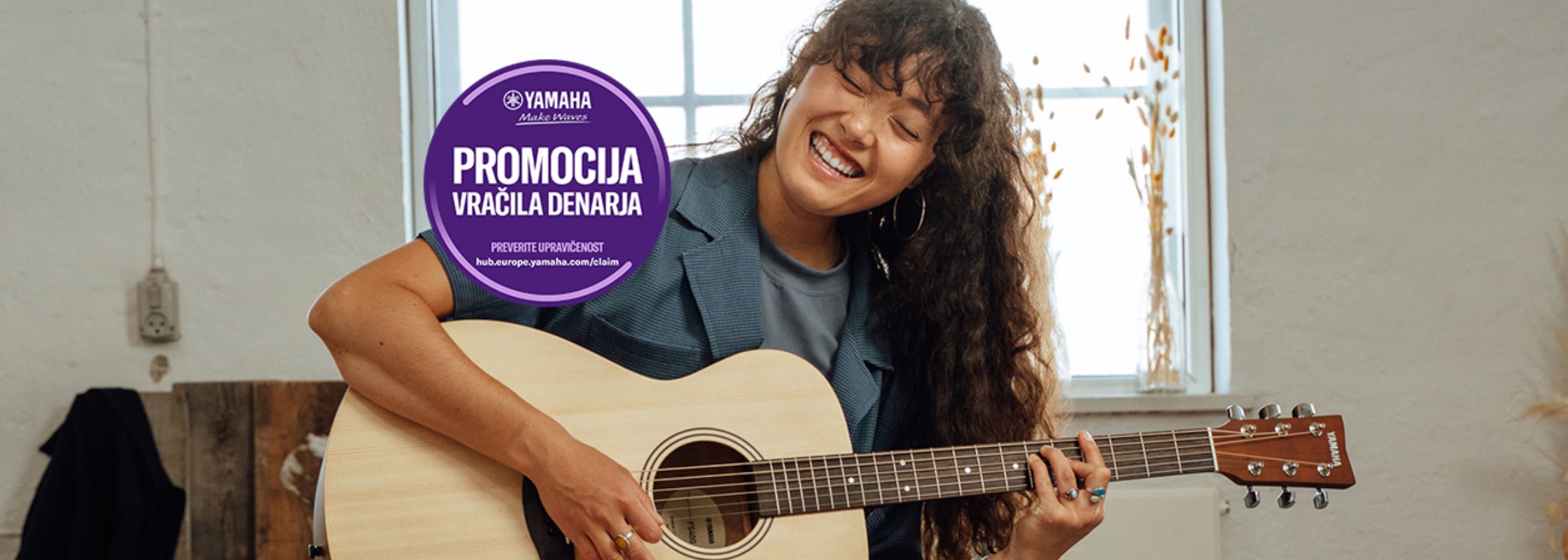 Smiling woman playing an acoustic guitar indoors, with a purple circular promotional sticker on the guitar neck area.