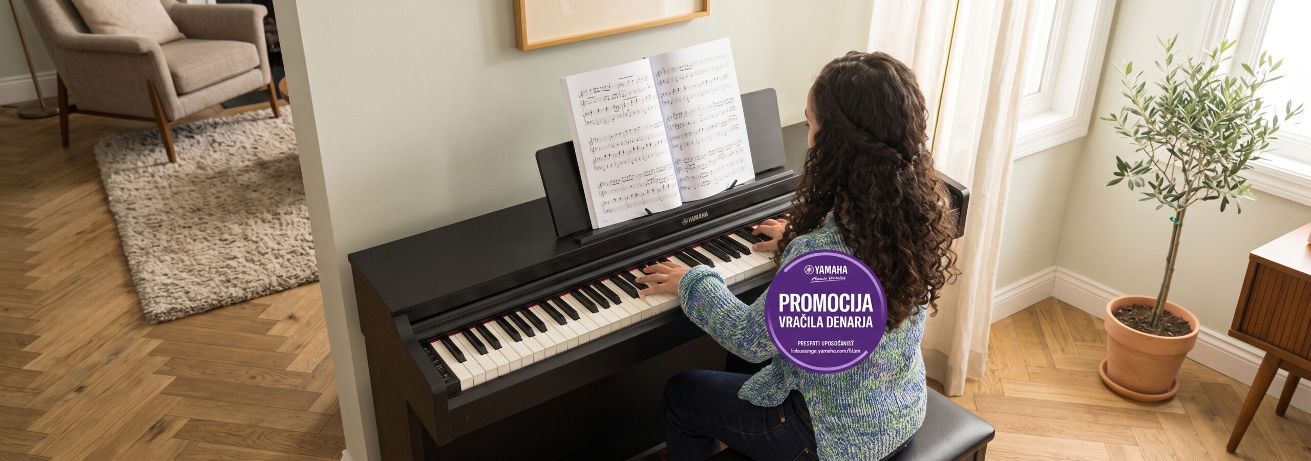 Young woman with curly hair plays a Yamaha digital piano at home; a large purple promo sticker on her back reads 'PROMOCIJA VRACILA DENARJA'.